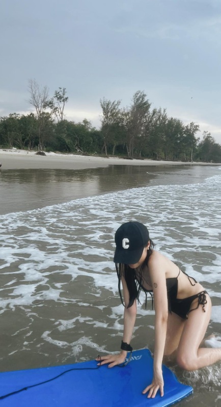 小桃在沙巴海邊雙手扶著藍色浮板，準備登上板面。